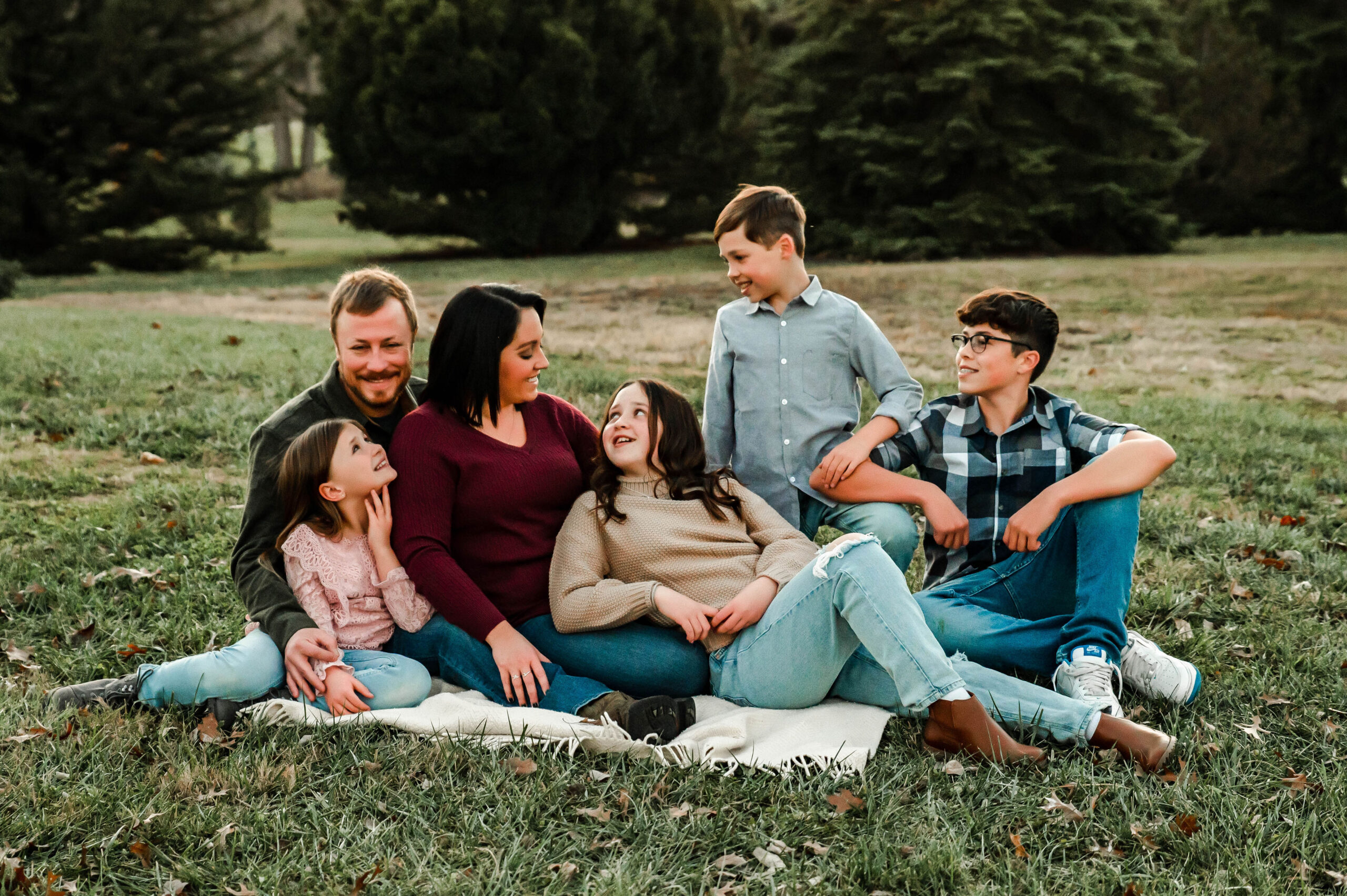 Family sitting together in the park looking at one another smiling. Family photos in Cincinnati.