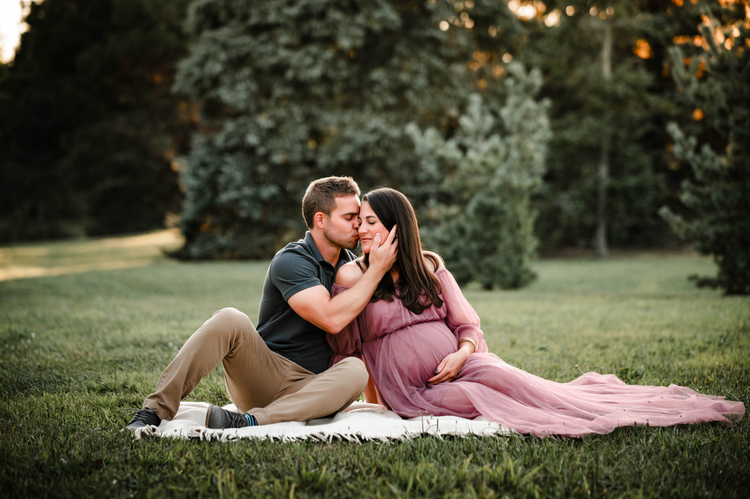 Pregnant Couple sitting in the park loving on one another woman in pink maternity gown utilizing services of a doula in dayton, oh