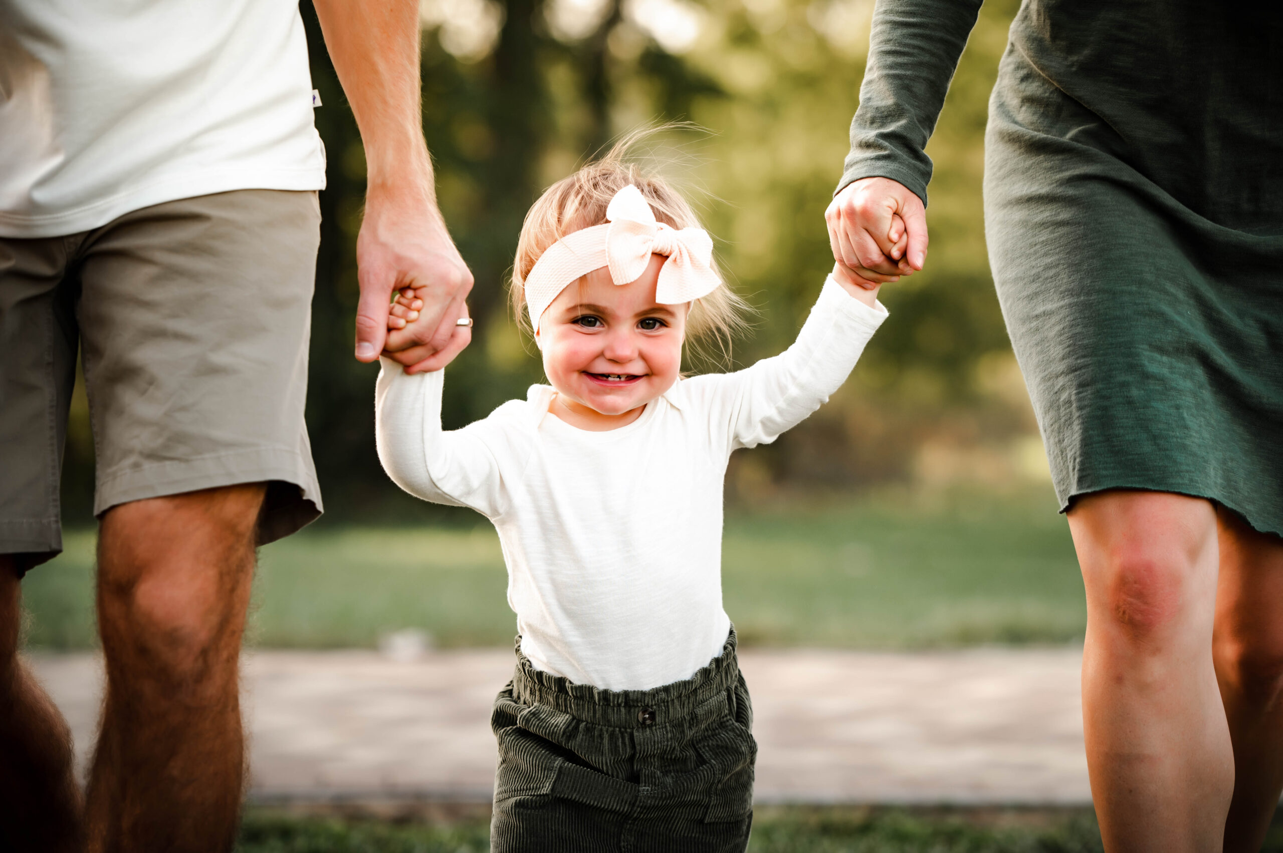 Toddler holding mom and dads hands smiling at the park in Dayton oh