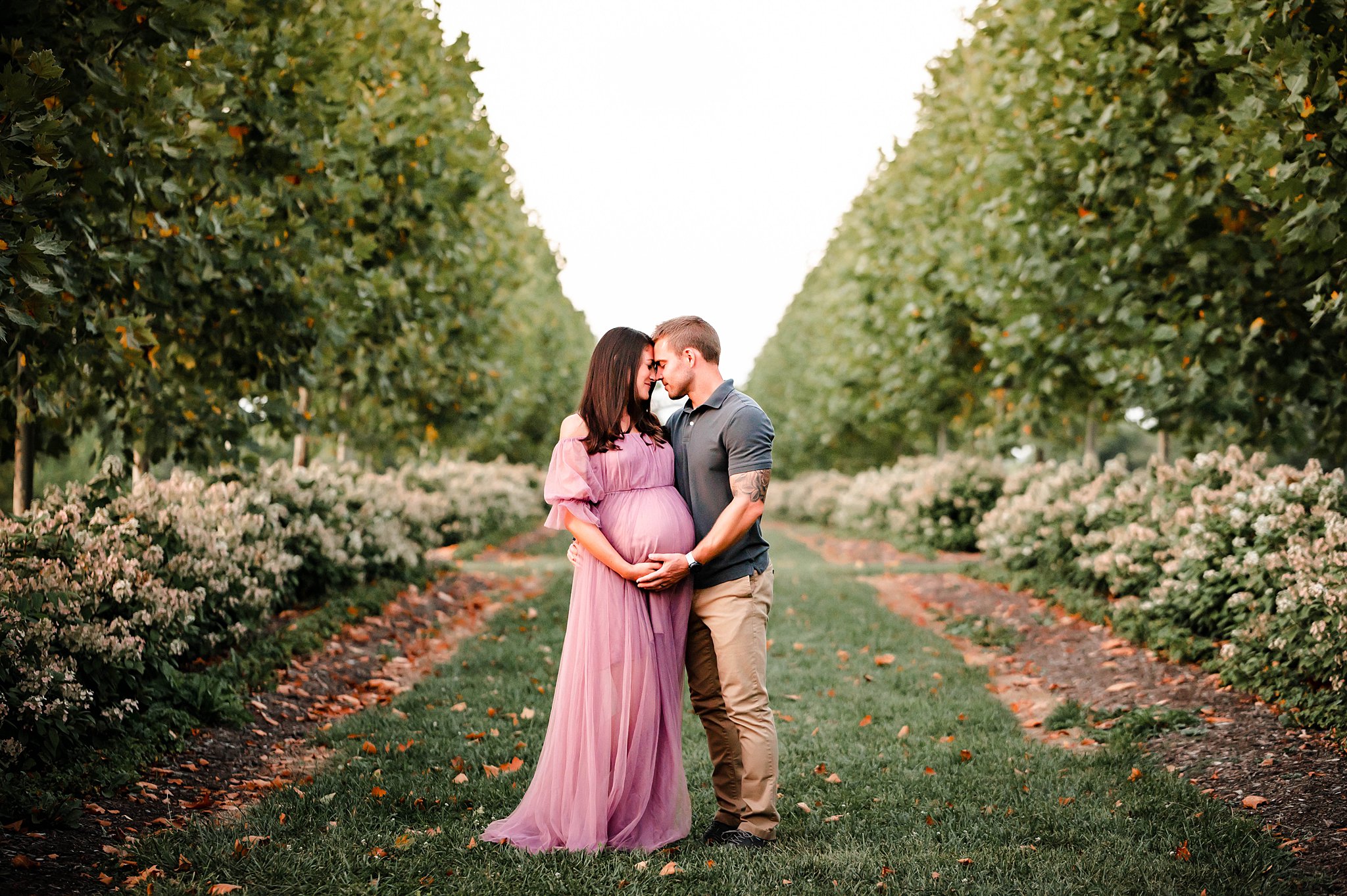 mom to be in a pink maternity gown and her husband standing in a garden midwife dayton ohio