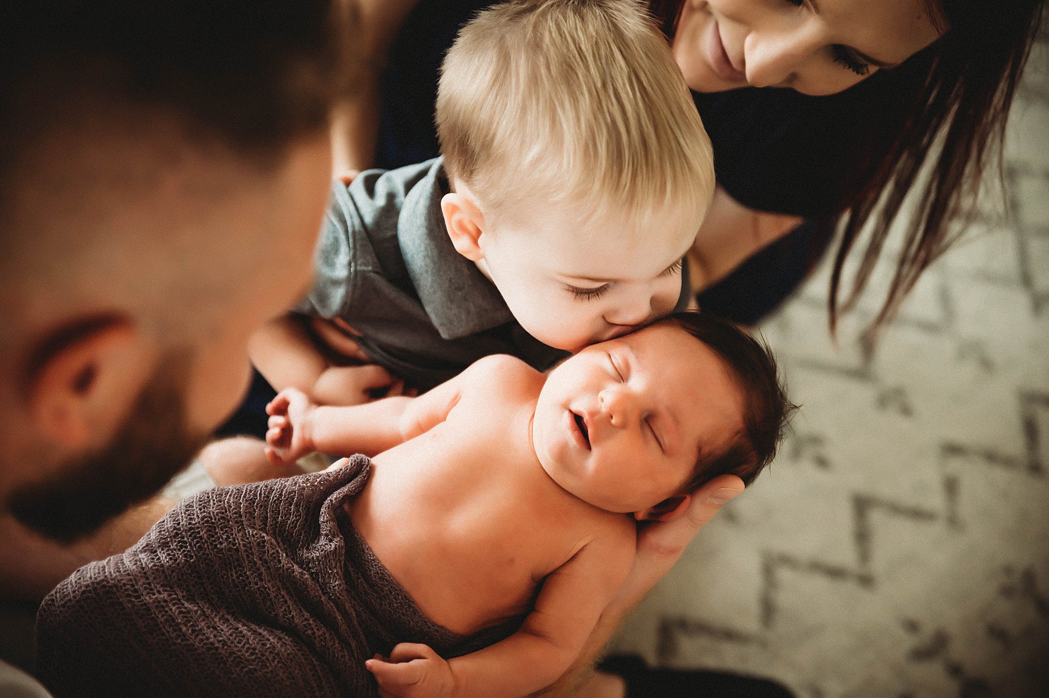 little boy kissing his newborn sibling on the cheek