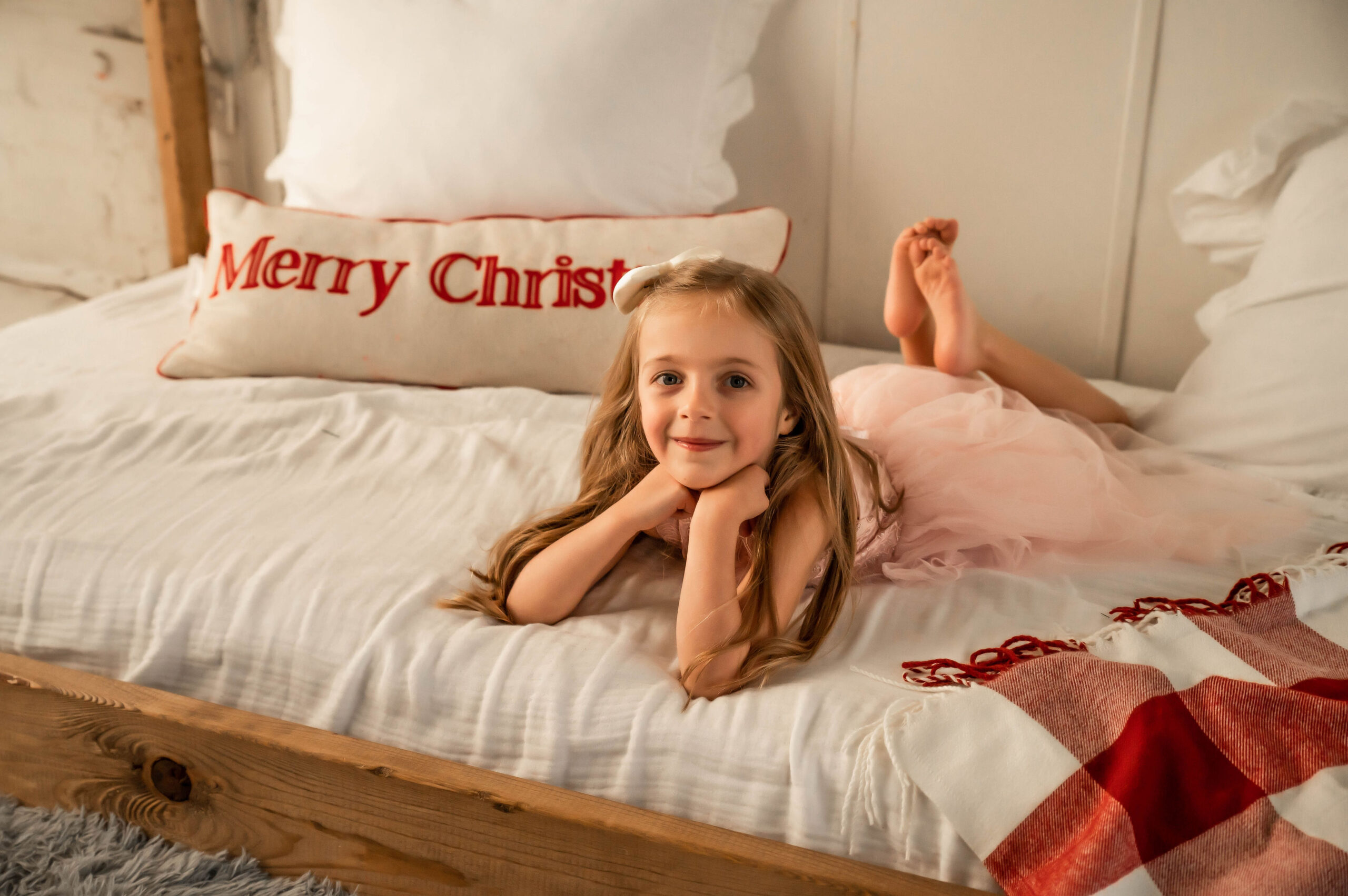 Little girl in tutu, laying on a Merry Christmas wooden bed.