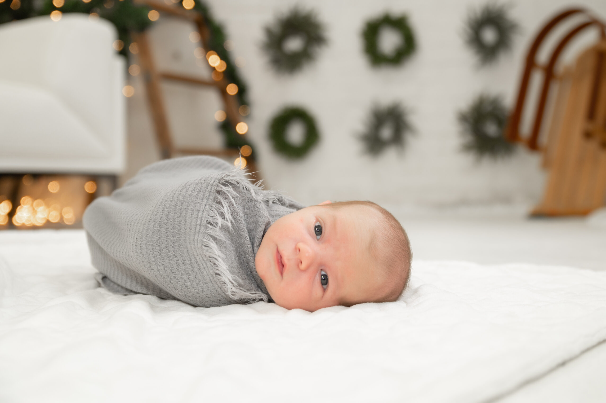 Newborn swaddled on cozy rug with Christmas wreath background.